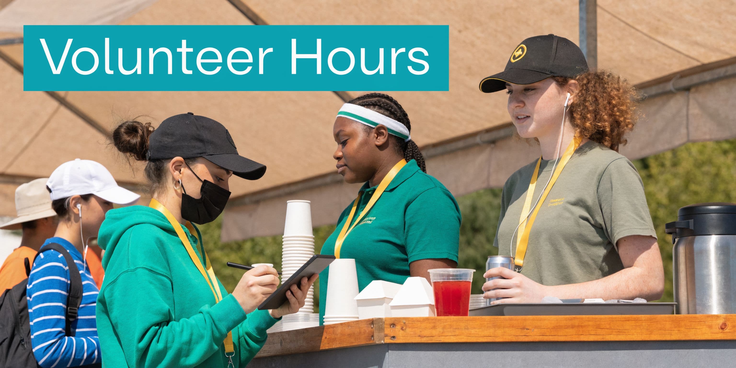Three volunteers working at a concession stand serving drinks and recording information on a tablet.