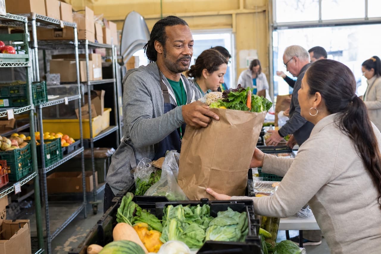 Food bank volunteer handing a bag of fresh groceries to a community member during distribution