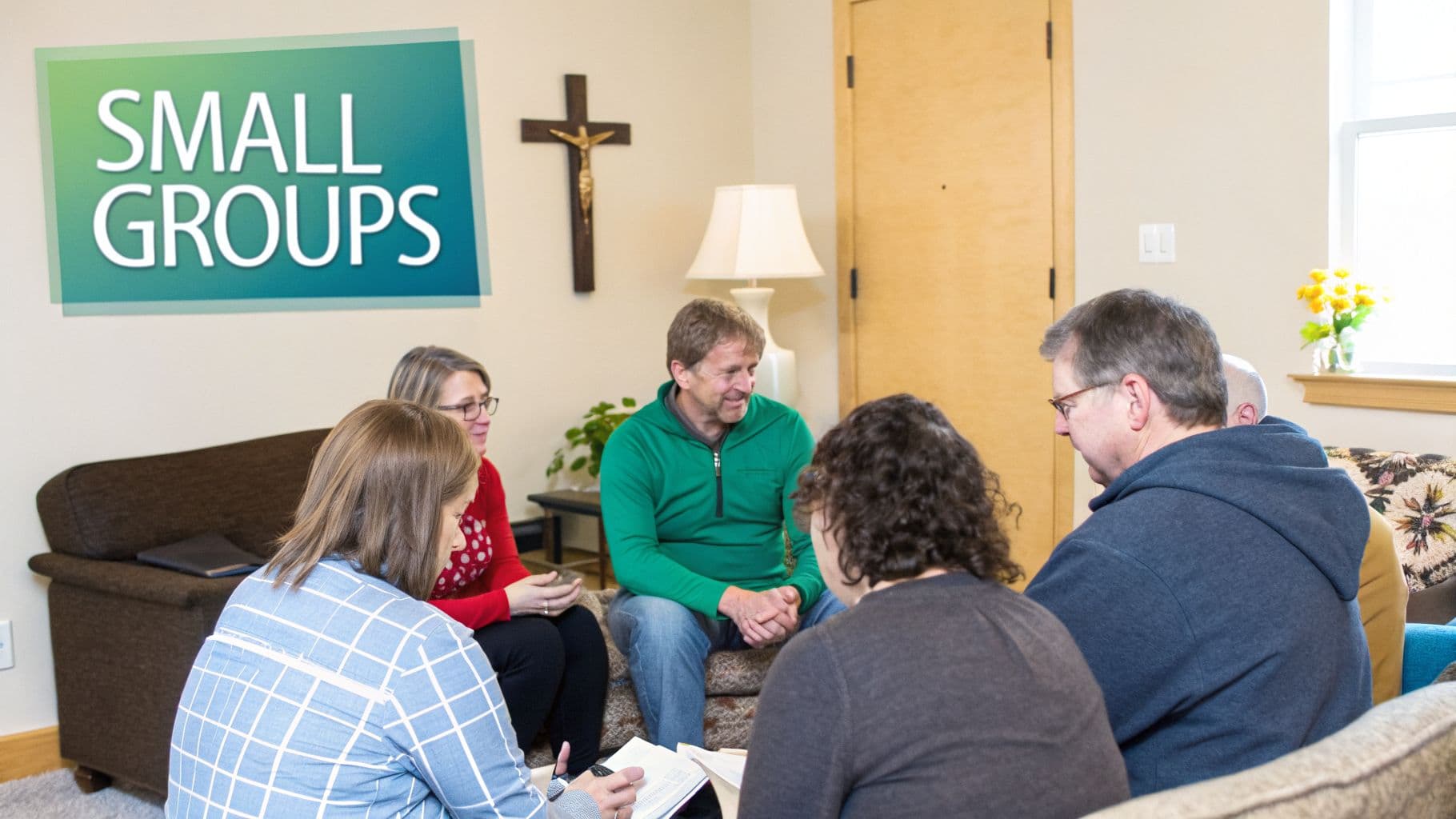 A diverse group of adults sitting in a circle, engaged in discussion during a small group meeting, with a Small Groups sign on the wall.