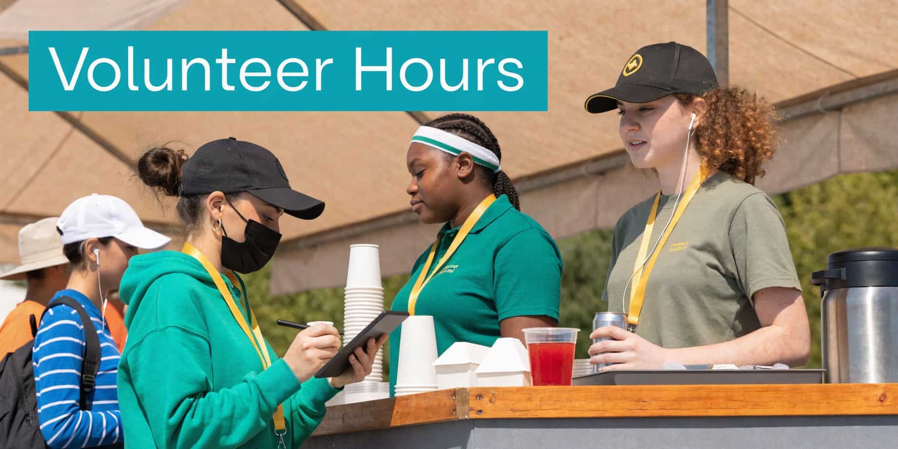 Three volunteers working at a concession stand serving drinks and recording information on a tablet.
