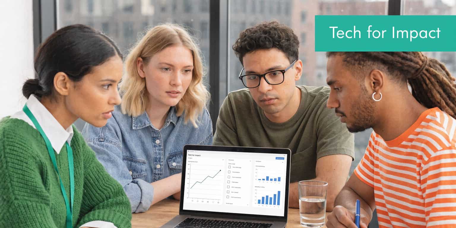 Diverse team of four professionals collaborate around a laptop discussing data charts on a screen.