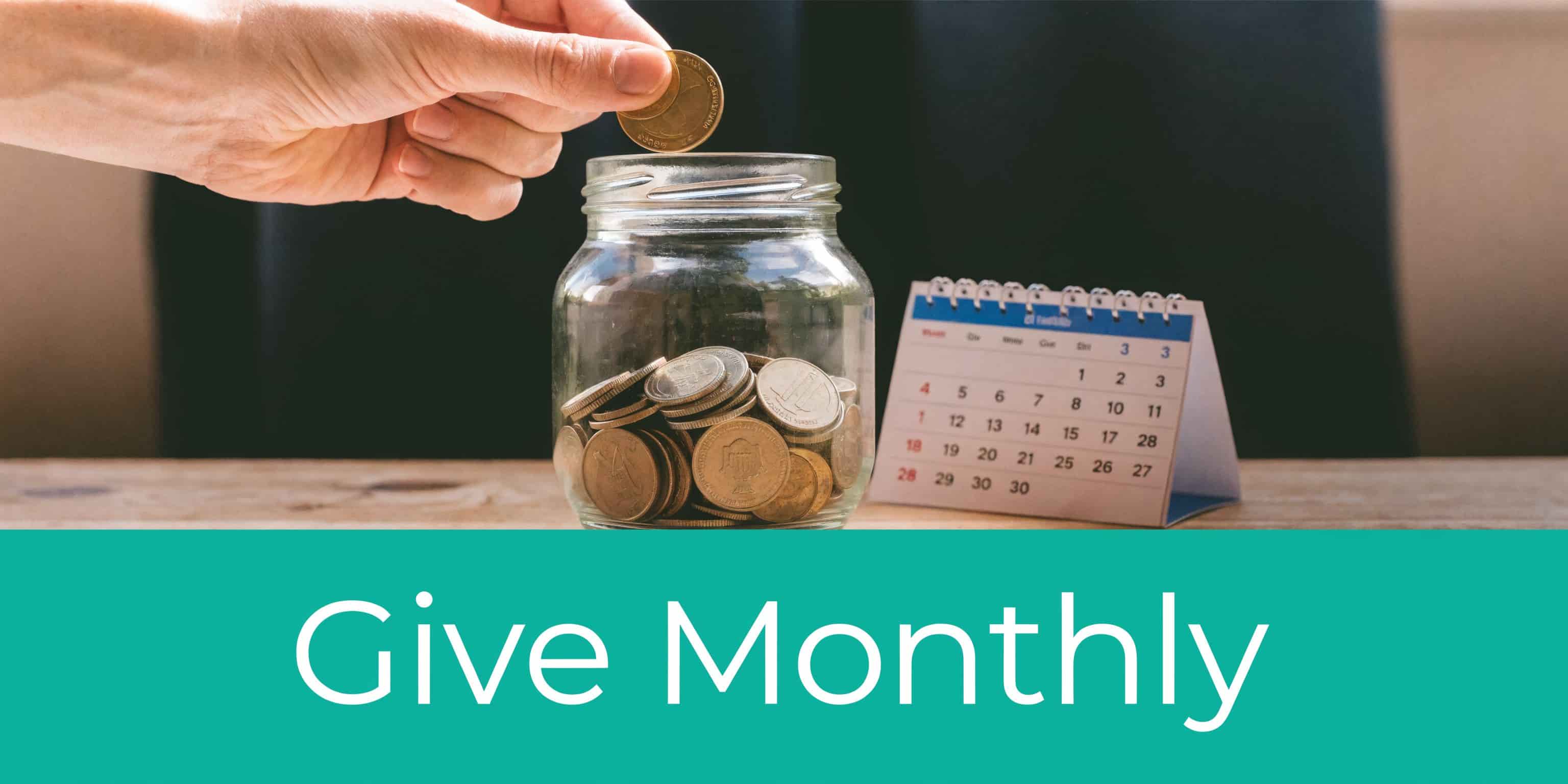 Hand placing a coin into a glass jar next to a calendar for monthly donations.